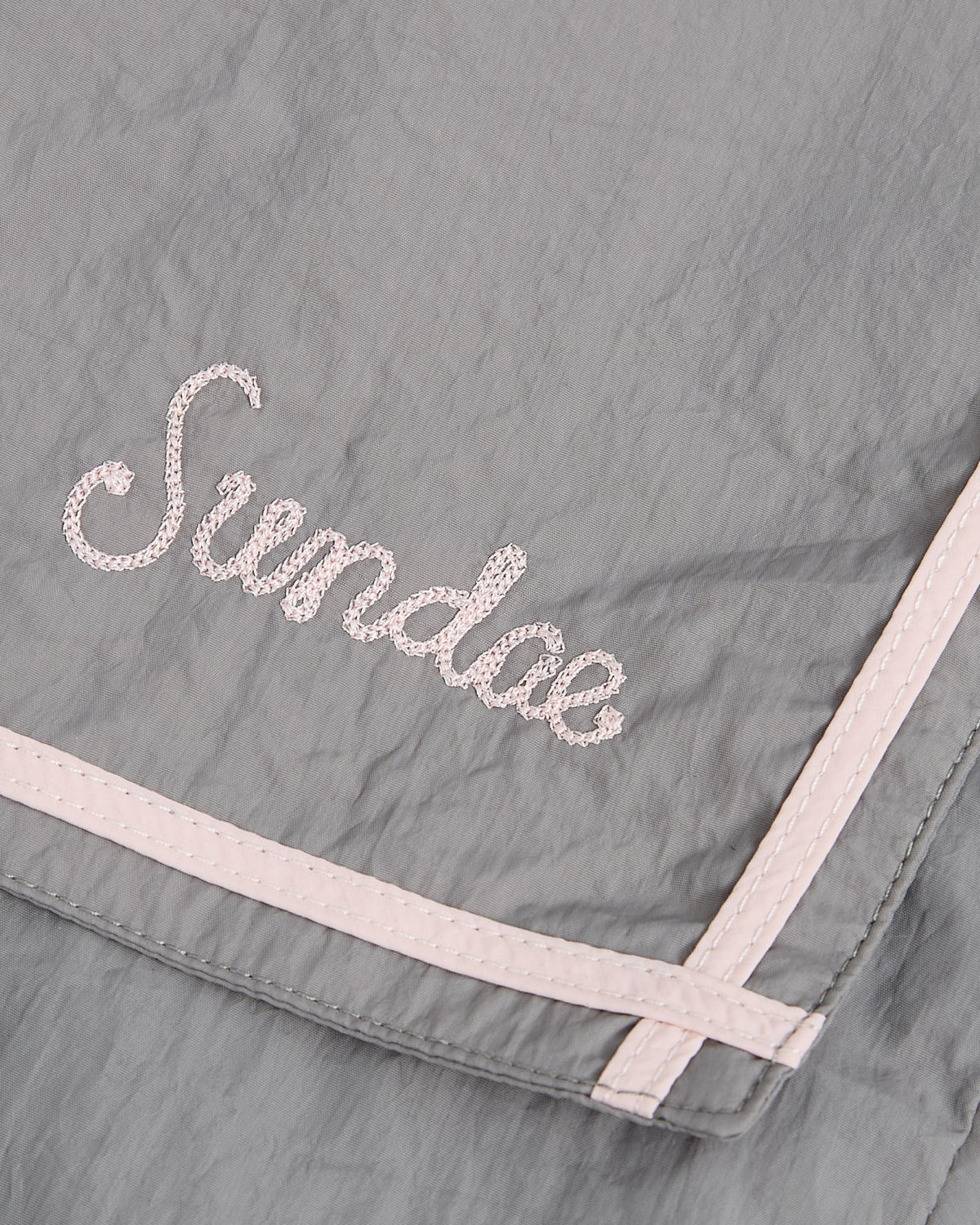 A gray fabric cropped windbreaker from Sundae School featuring light pink trim and “Sundae” embroidered in pink cursive lettering, called the GREY SAILOR WINDBREAKER.
