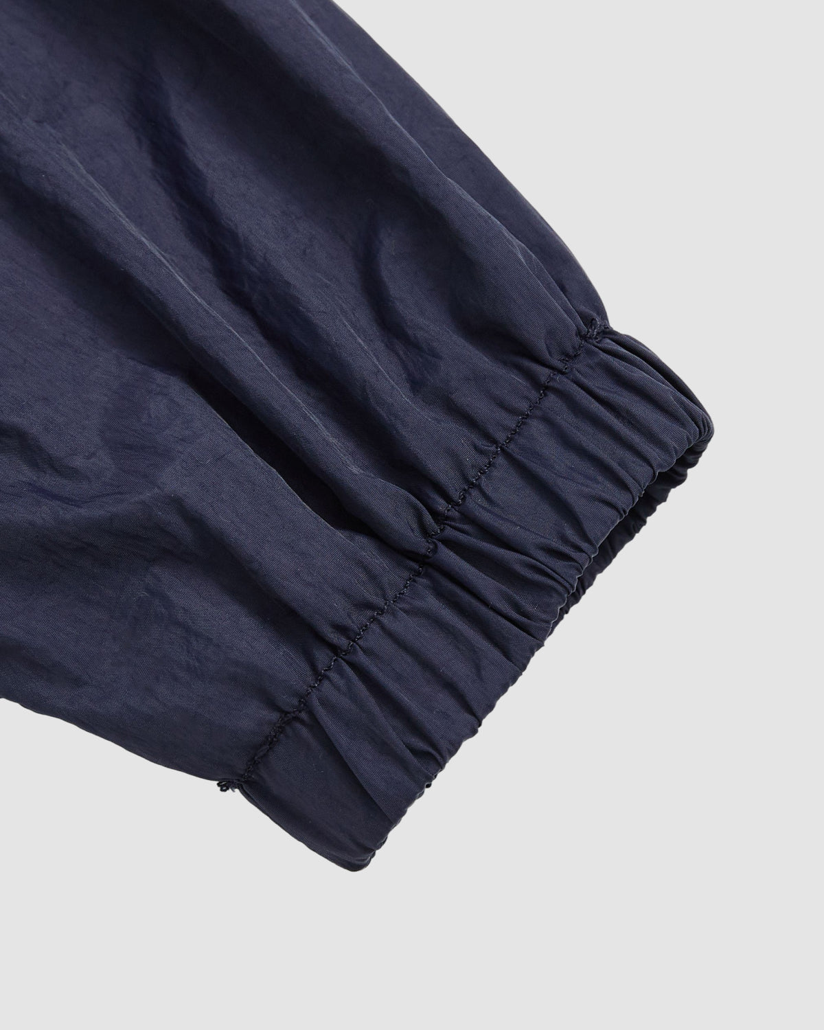 Close-up of the Sundae School NAVY SAILOR WINDBREAKER’s navy sleeve with elasticated cuff, crafted from lightweight, crinkled fabric, shown against a plain light gray background.