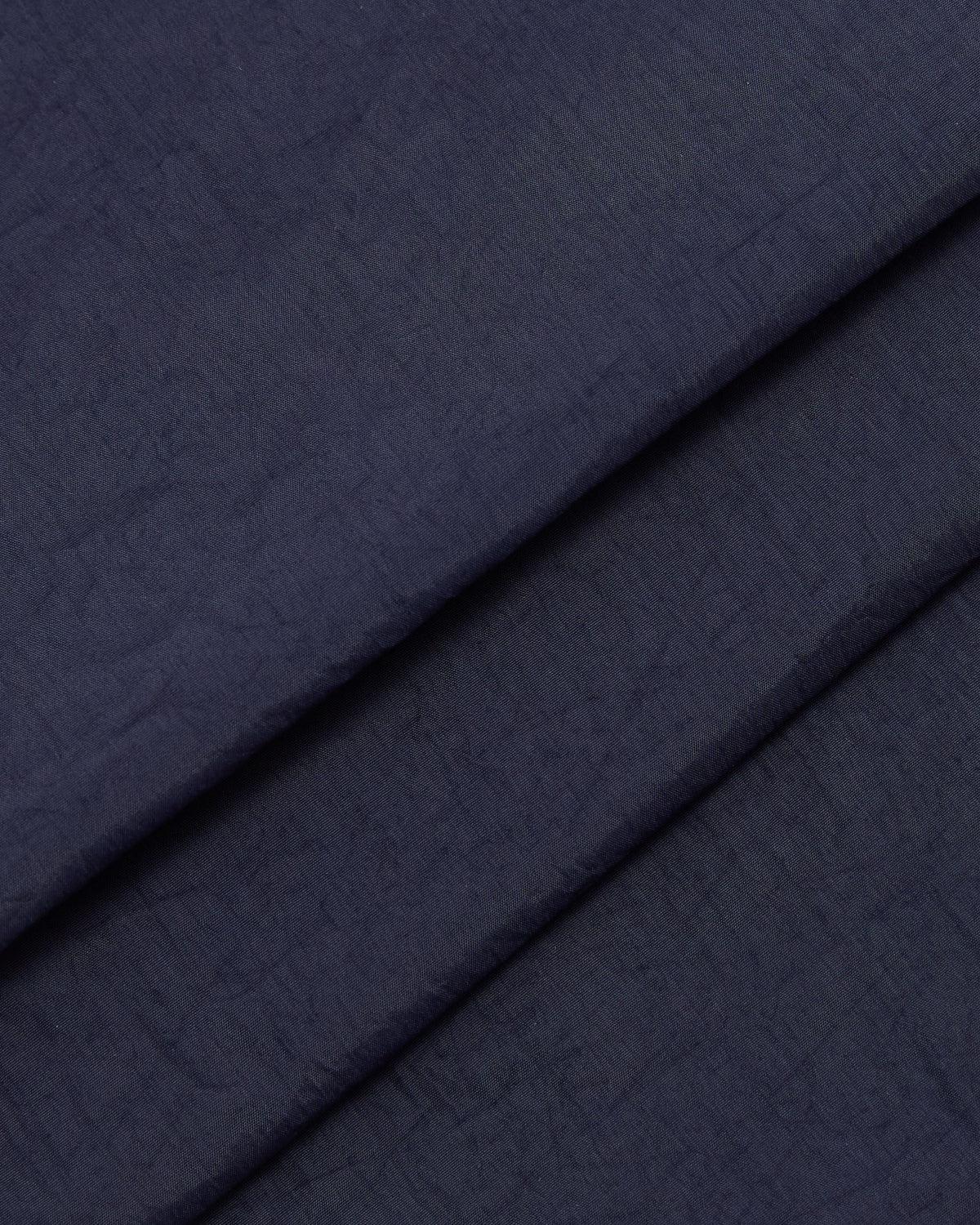 Close-up of Sundae School's NAVY SAILOR WINDBREAKER: folded dark navy fabric with a subtle textured surface, soft creases, and a matte finish reminiscent of a classic windbreaker.