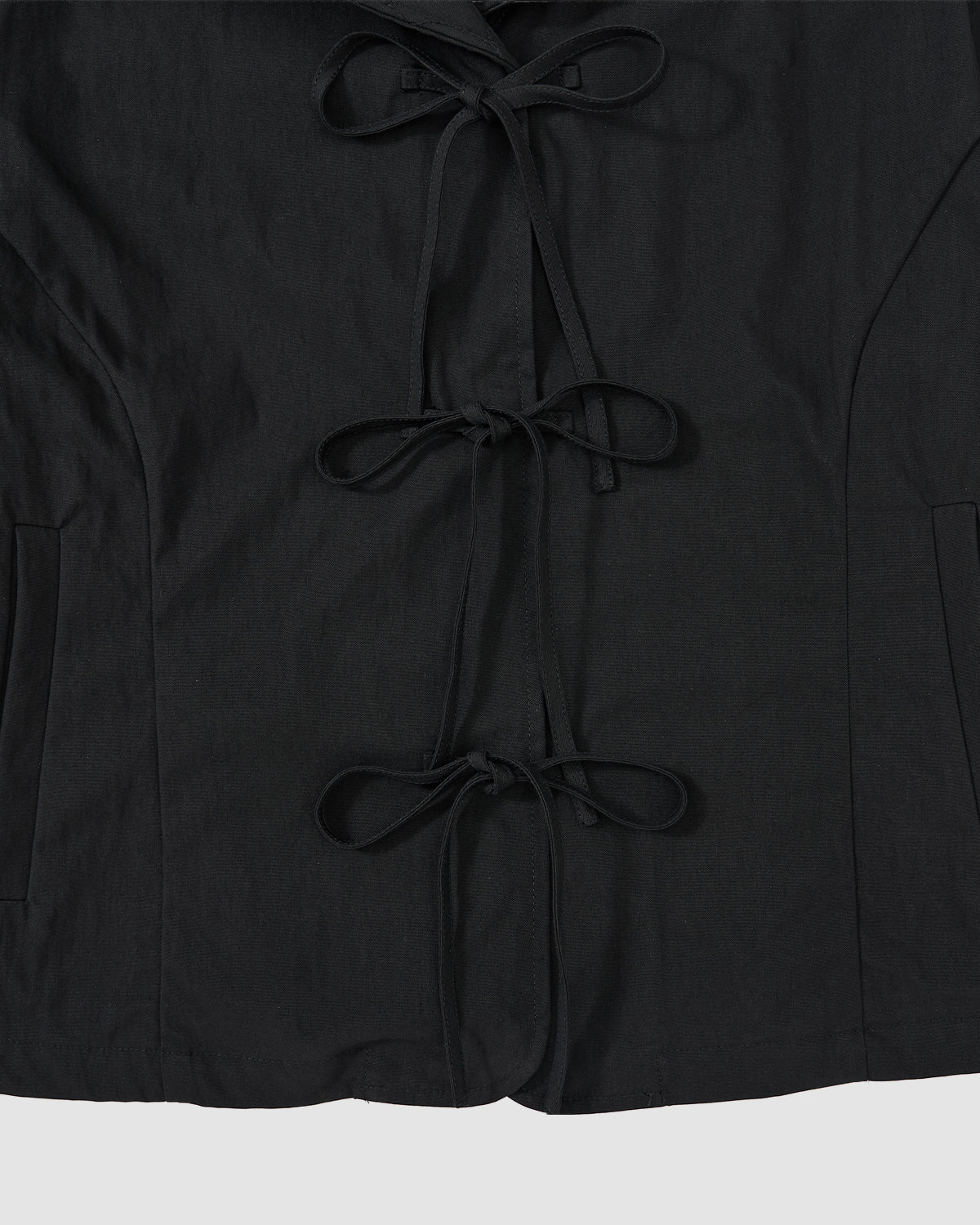 A close-up of the BLACK SAILOR COLLAR UNIFORM JACKET by Sundae School, showing three vertical fabric ties on the front, mochi quilted stitching, and partially visible side pockets.