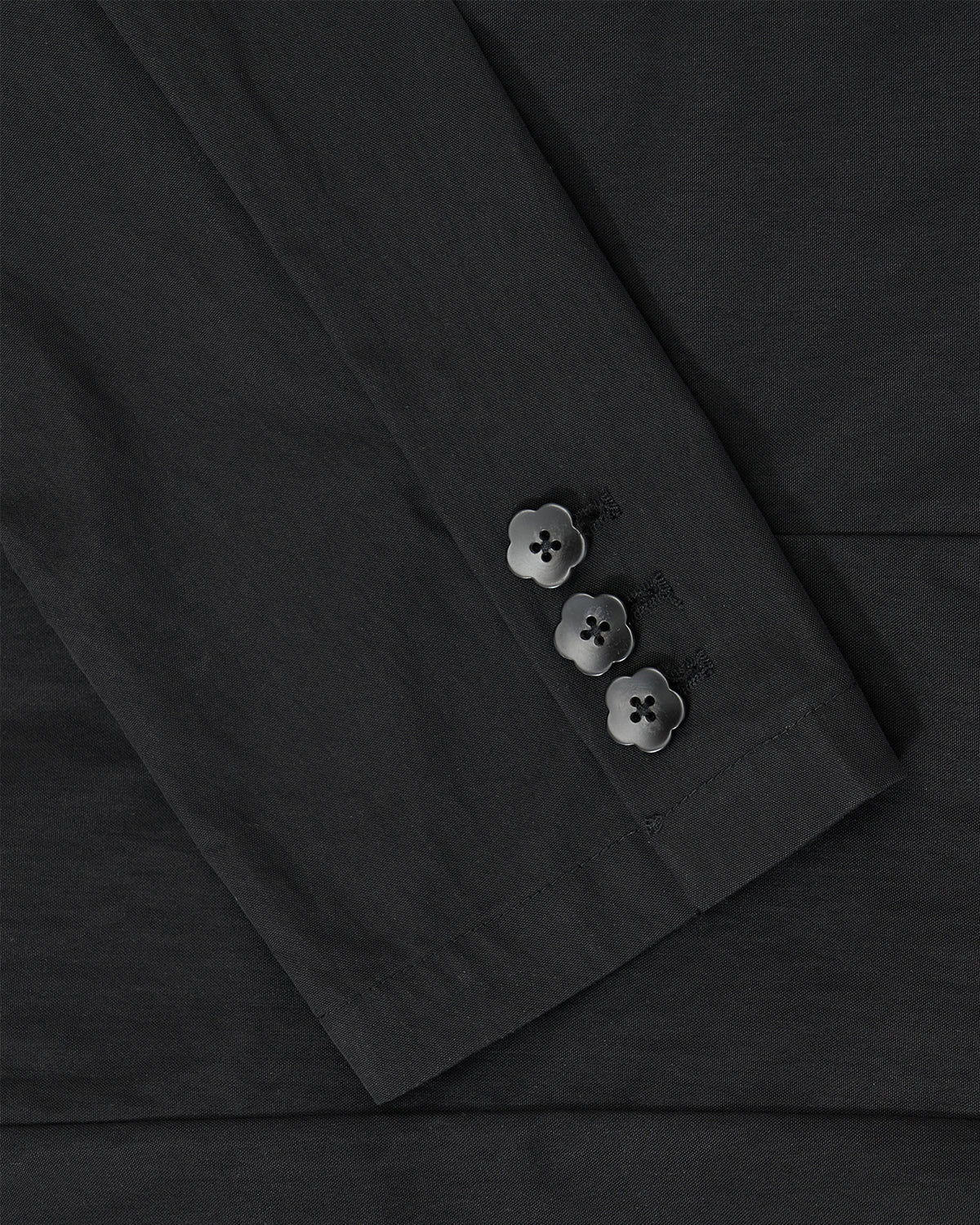 A close-up of the BLACK SAILOR COLLAR UNIFORM JACKET by Sundae School shows three black flower-shaped buttons on the sleeve cuff, arranged diagonally against matching fabric, evoking classic Korean school uniform style.