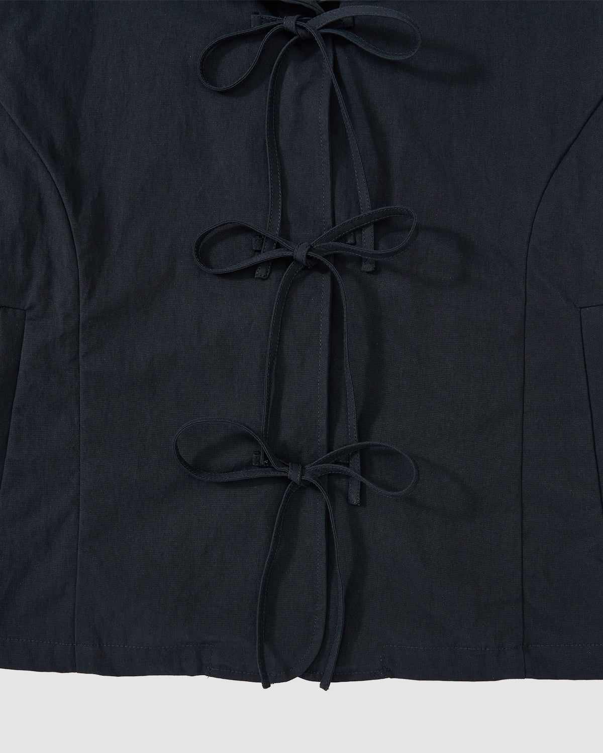 Close-up of Sundae School's NAVY SAILOR COLLAR UNIFORM JACKET in black, featuring three fabric bow ties down the front, visible seams, and curved side panel design.