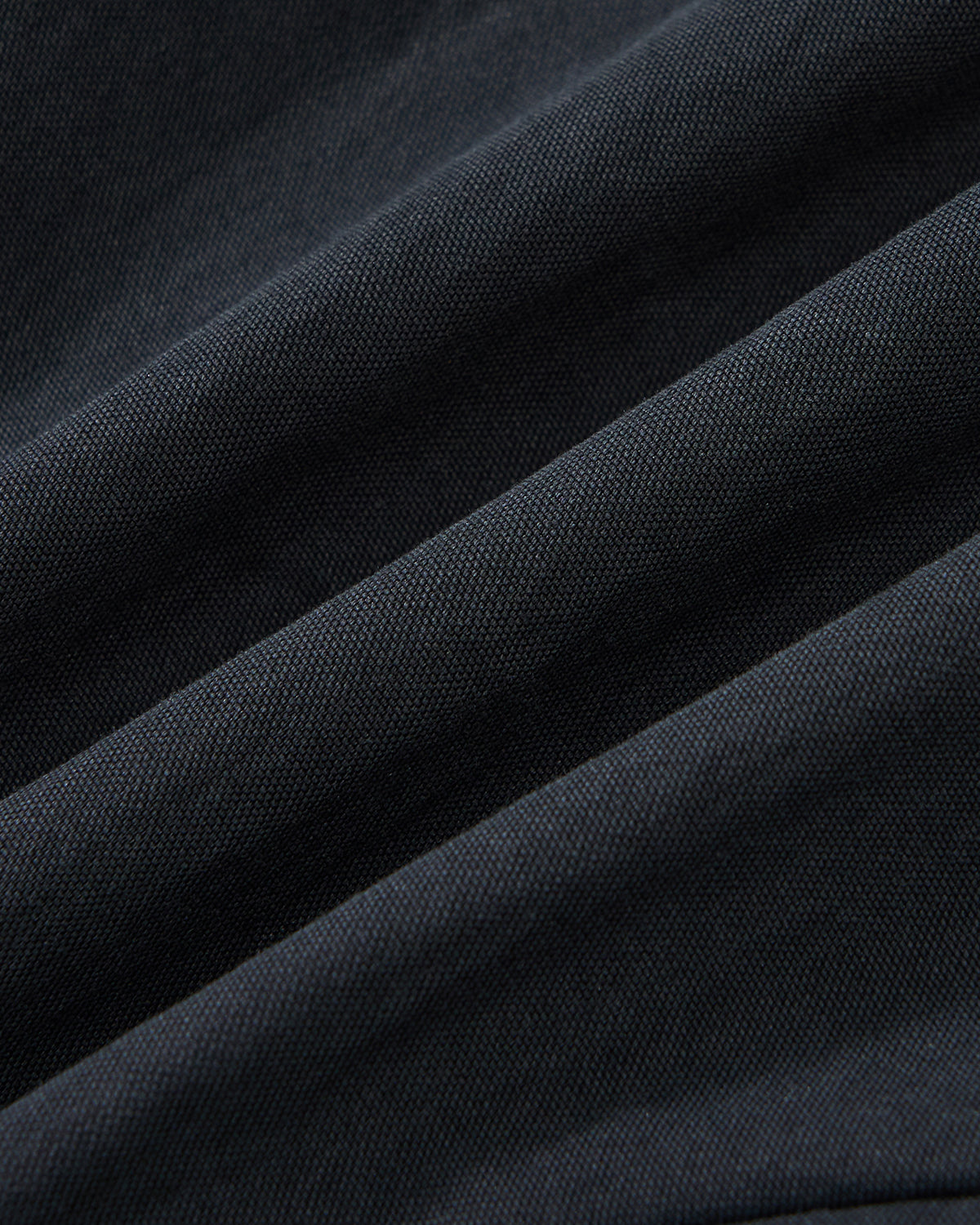Close-up of Sundae School's NAVY SAILOR COLLAR UNIFORM JACKET shows dark, textured fabric with diagonal folds and a fine weave, highlighted by soft lighting that accentuates its subtle matte finish.