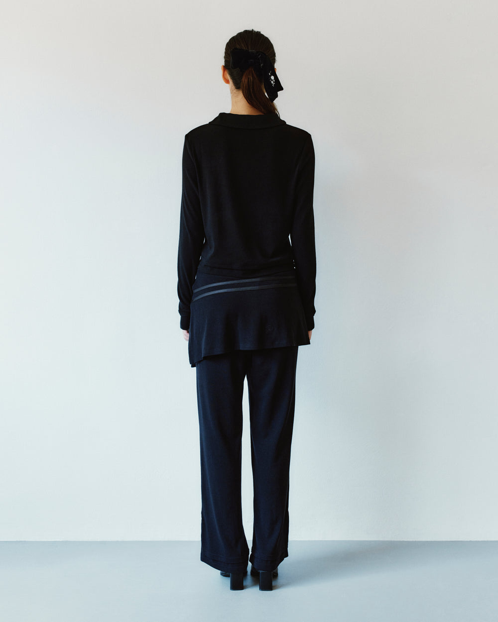 Back view of a person wearing a black rounded collar BLACK SEONGSU KEYHOLE TOP with a back keyhole detail and matching trousers.