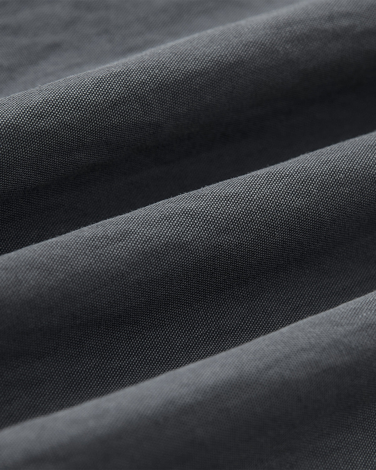 Close-up of the CHARCOAL SHAWL COLLAR ANORAK by Sundae School, featuring dark gray fabric with a fine, textured weave and soft folds, echoing monk-core style.