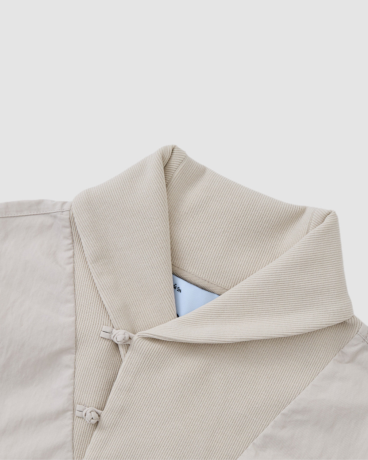 Close-up of the IVORY SHAWL COLLAR ANORAK by Sundae School, featuring a textured ribbed shawl collar and two fabric knot closures on the front, shown against a white background.