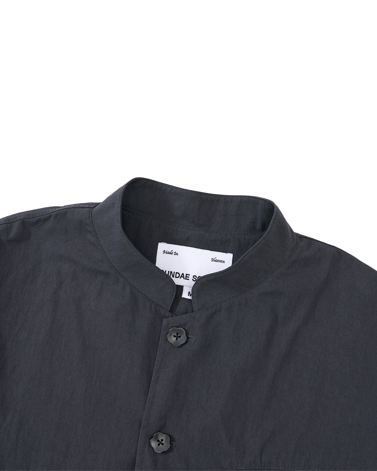 A close-up of the Sundae School CHARCOAL STAND COLLAR UNIFORM JACKET, made from a soft cotton-nylon blend with two buttons, set against a light grey background. A white label is visible inside the collar.