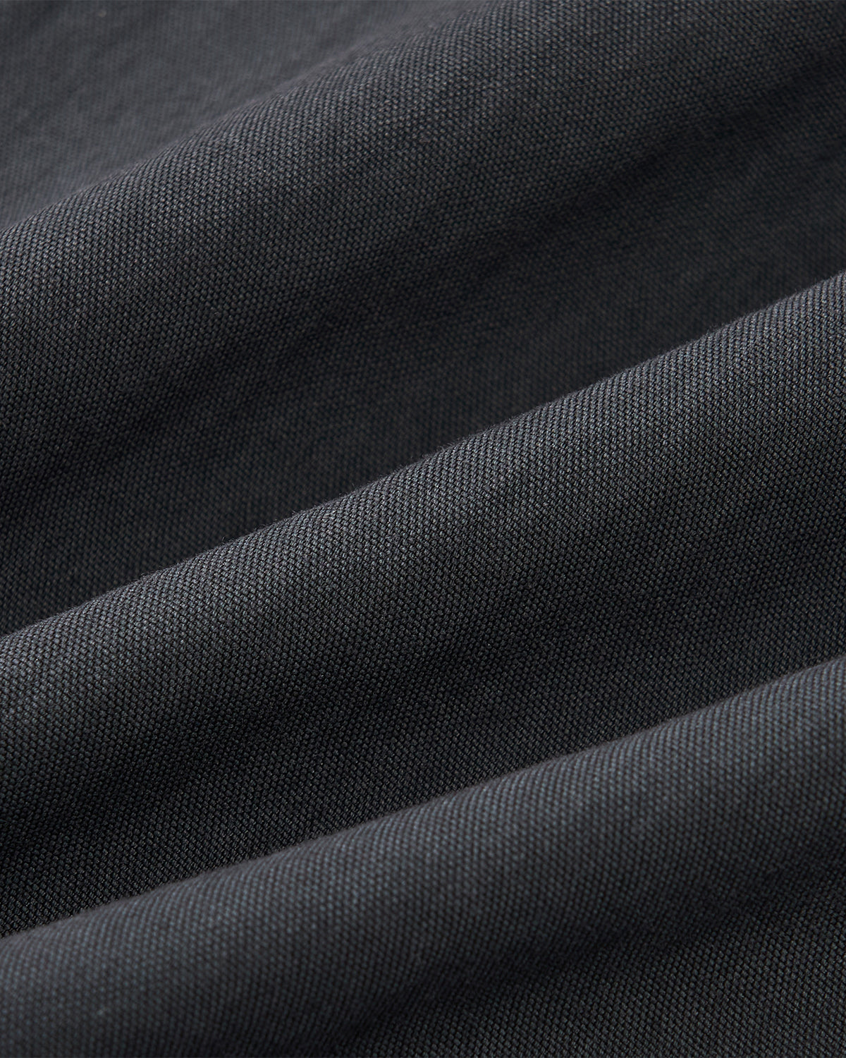 Close-up of charcoal cotton-nylon blend fabric with visible weave and soft folds, forming diagonal lines and subtle shadows—perfect for the CHARCOAL STAND COLLAR UNIFORM JACKET by Sundae School.
