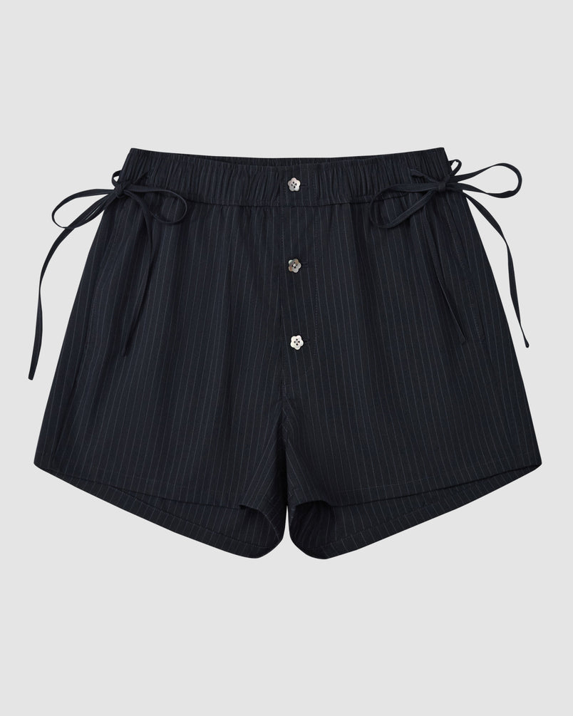 The Sundae School NAVY STRIPE BOXER SHORTS feature a pinstripe design, elastic waistband, side ties, and three front buttons. Crafted from a soft Tencel-rayon blend, the shorts are shown laid flat on a plain light gray background.