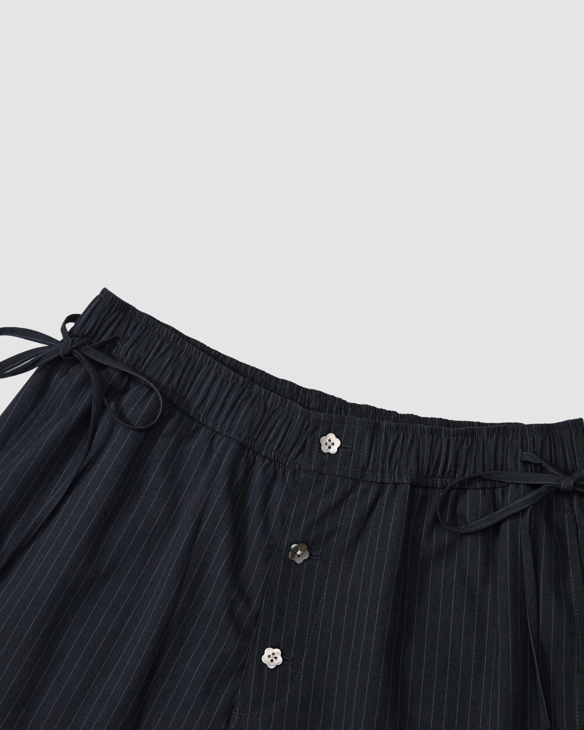 Close-up of Sundae School NAVY STRIPE BOXER SHORTS in dark pinstripes, crafted from a soft Tencel-rayon blend with an elastic waistband, side drawstrings, and front buttons—perfect for stylish work-from-home comfort against a light gray background.