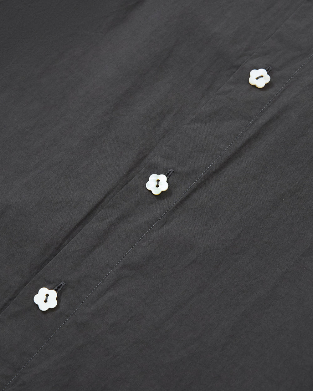 Close-up of the CHARCOAL SUNBAE TIE SHIRT by Sundae School, featuring black fabric adorned with four small, white flower-shaped buttons arranged in a vertical line.