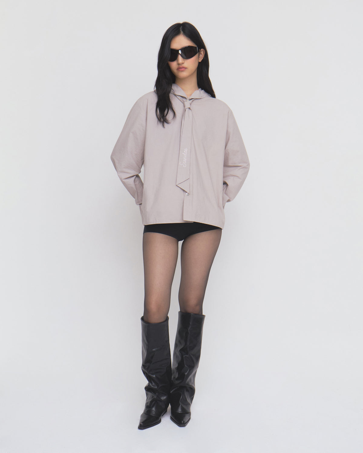 Model in black sunglasses, the Sundae School GREY SUNBAE TIE SHIRT, black shorts, sheer black tights, and black knee-high boots stands against a plain white background.