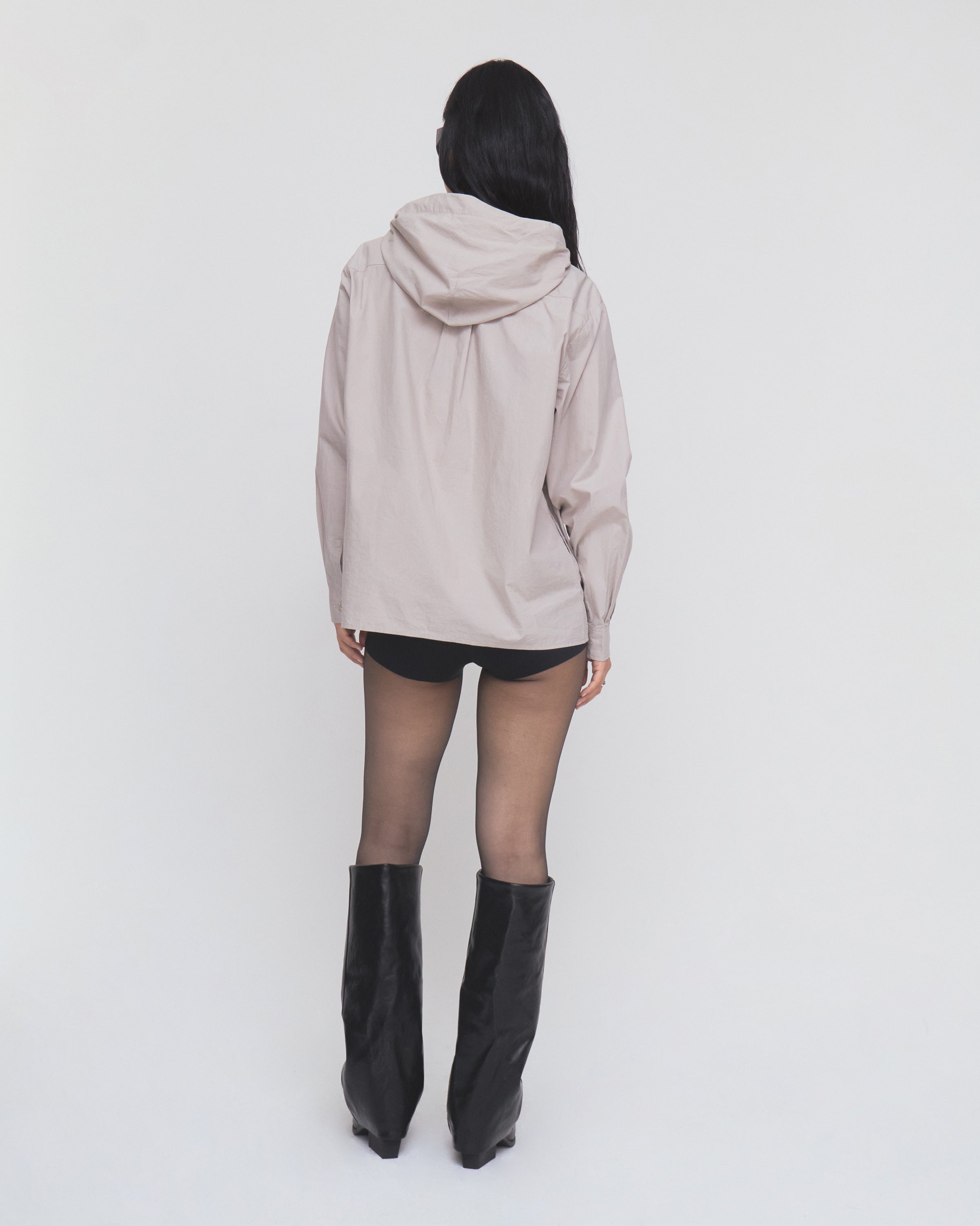 A person stands against a plain white background, facing away from the camera, wearing the GREY SUNBAE TIE SHIRT by Sundae School, paired with black shorts, sheer tights, and black knee-high boots.