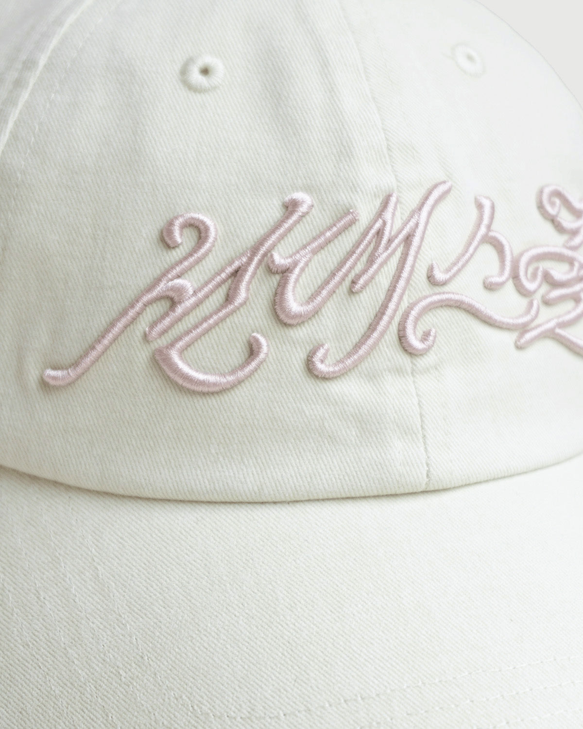 Close-up of the Sundae School IVORY DAENGGI CAP, a white adjustable cotton cap featuring light pink embroidered cursive lettering across the front. Only part of the text is visible in the image.