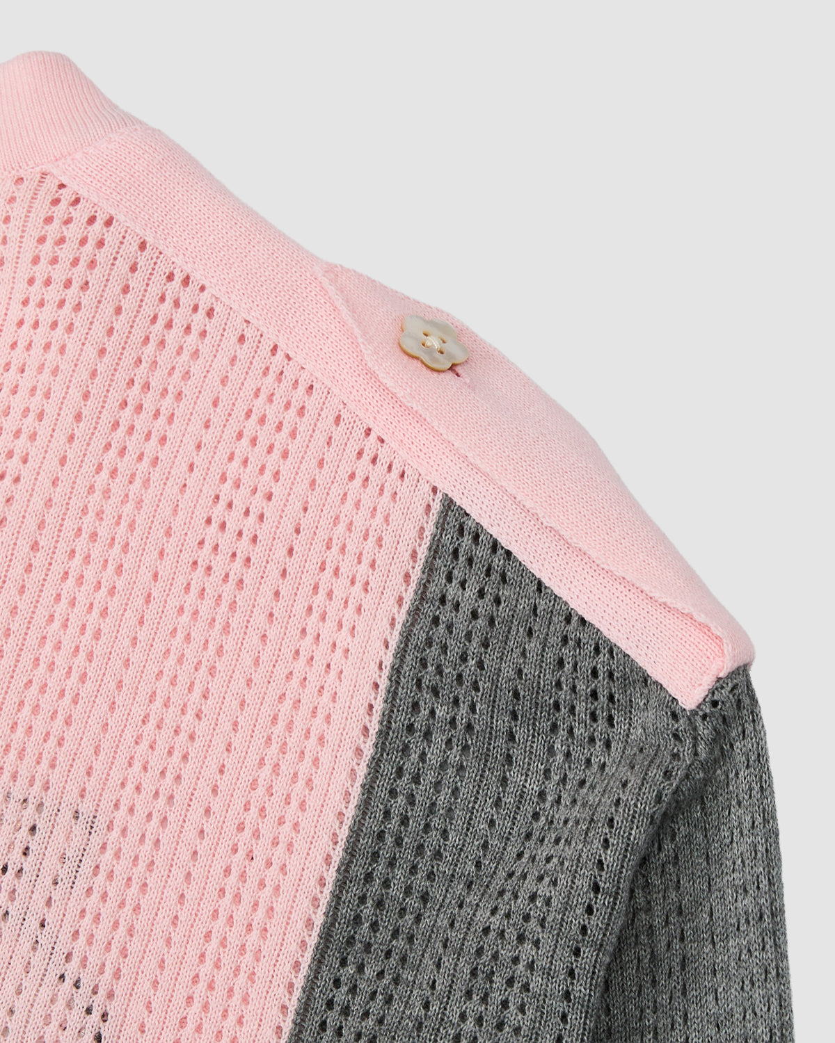 Close-up of the PINK SUNDAE SOCCER JERSEY by Sundae School, crafted from 100% cotton with lightweight pink and gray panels. The jersey features a textured perforated knit pattern and is accented with a single beige button on the pink shoulder area.