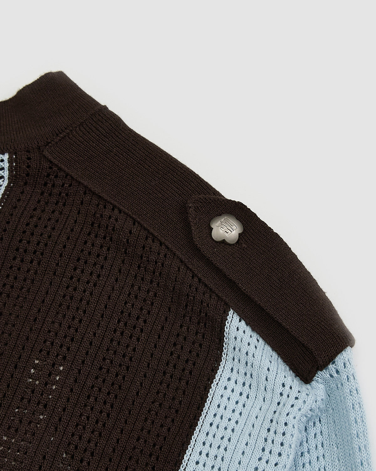 Close-up of Baby Blue Brown Sundae Soccer Jersey Knit shoulder seam and snap button detail on brown knit fabric, showing construction quality and white flower-shaped hardware finish with ribbed texture contrast between different knit sections.