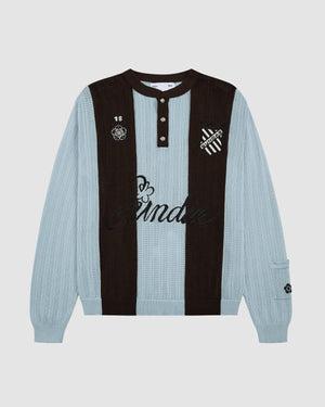Baby Blue Brown Sundae Soccer Jersey Knit flat lay featuring vertical stripes in light blue and brown ribbed knit construction, henley-style button placket with white snap buttons, "Sundae" script embroidery across chest with decorative hibiscus flower accent, "18" number patch and floral crest on left chest, striped shield logo on right chest, displayed on light grey background.