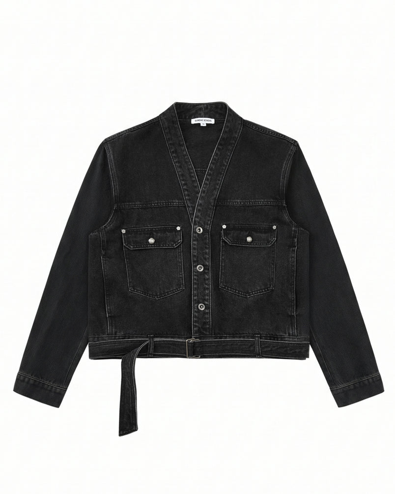 The BLACK WIDOW TAEKWONDO DENIM JACKET by Sundae School—a black, collarless V-neck denim jacket featuring a button front, double-buckle belt at the waist, and two flap chest pockets—offers a modern twist on the Korean Canadian tuxedo, shown here laid flat on a white background.