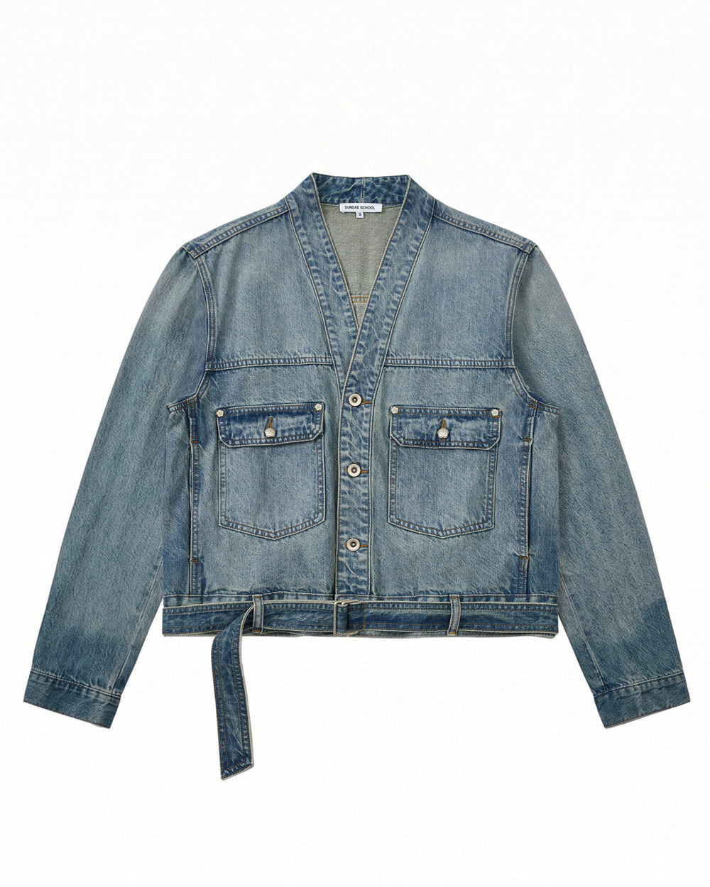 The MEDIUM BLUE TAEKWONDO DENIM JACKET by Sundae School features long sleeves, a V-neck collar, two front buttoned pockets, a button-down front, and a detachable waist belt—ideal for crafting your own Korean Canadian tuxedo look. Shown here laid flat on a white background.