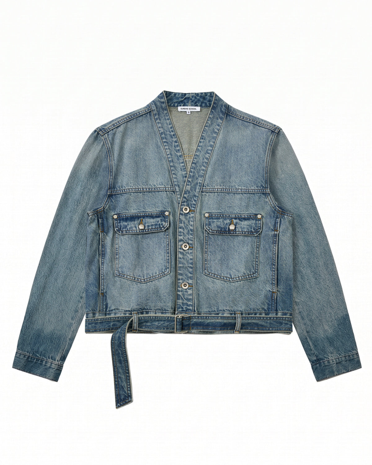 The MEDIUM BLUE TAEKWONDO DENIM JACKET by Sundae School features long sleeves, a V-neck collar, two front buttoned pockets, a button-down front, and a detachable waist belt—ideal for crafting your own Korean Canadian tuxedo look. Shown here laid flat on a white background.