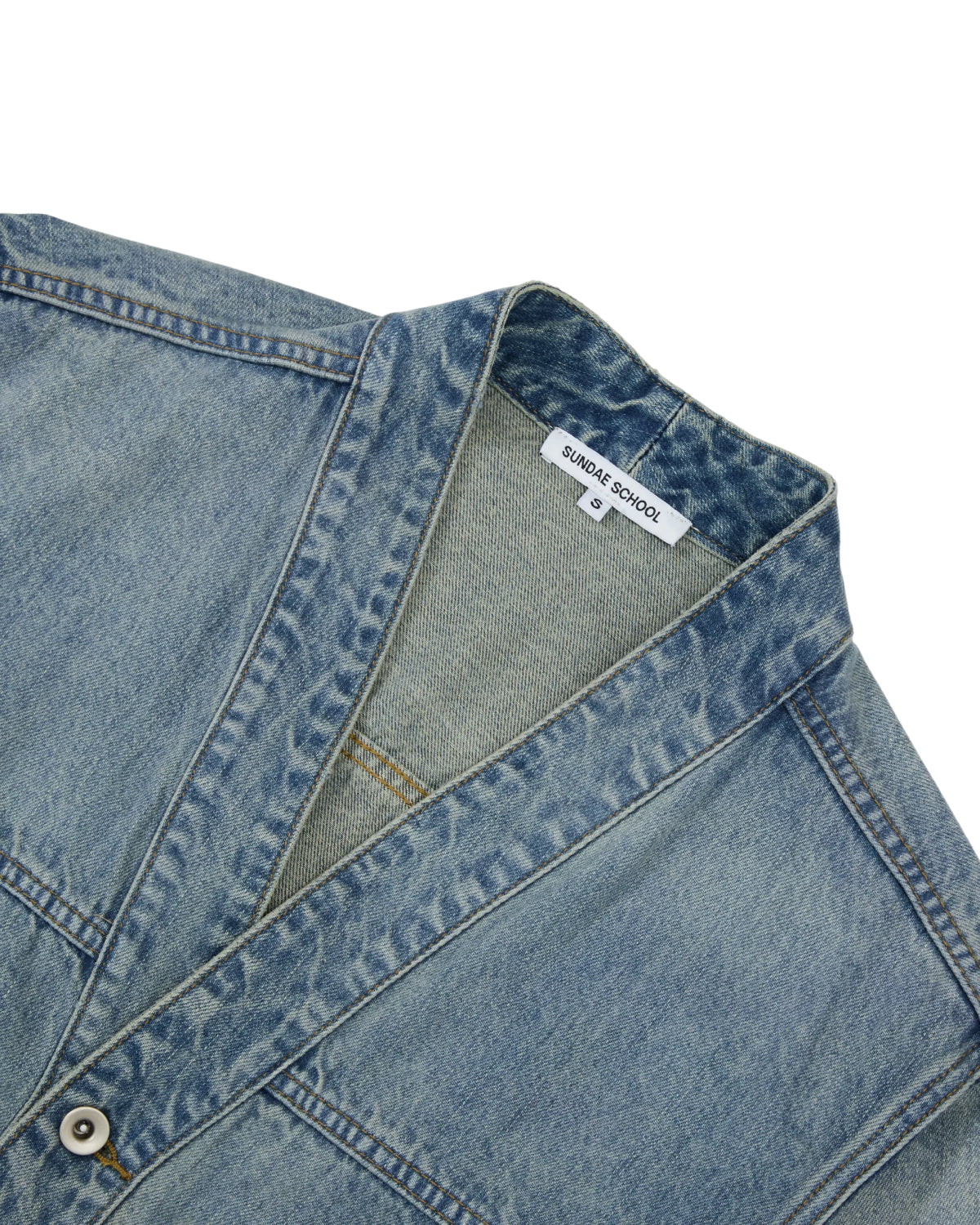 A close-up of the MEDIUM BLUE TAEKWONDO DENIM JACKET by Sundae School, showcasing a v-neck collar, white button, distinctive stitching, and a Sundae School label—embodying the effortlessly cool style of a Korean Canadian tuxedo.