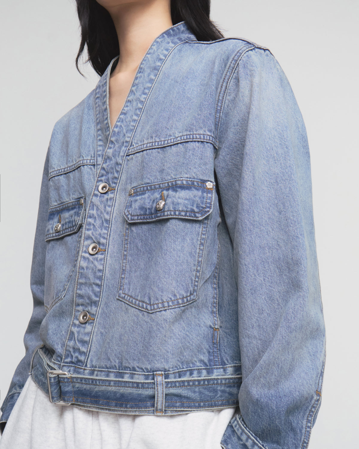 A person wears the Sundae School MEDIUM BLUE TAEKWONDO DENIM JACKET, styled in a classic Korean Canadian tuxedo look with buttoned chest pockets and a V-neckline, layered over a white top. The image shows the individual from shoulders to waist against a plain background.