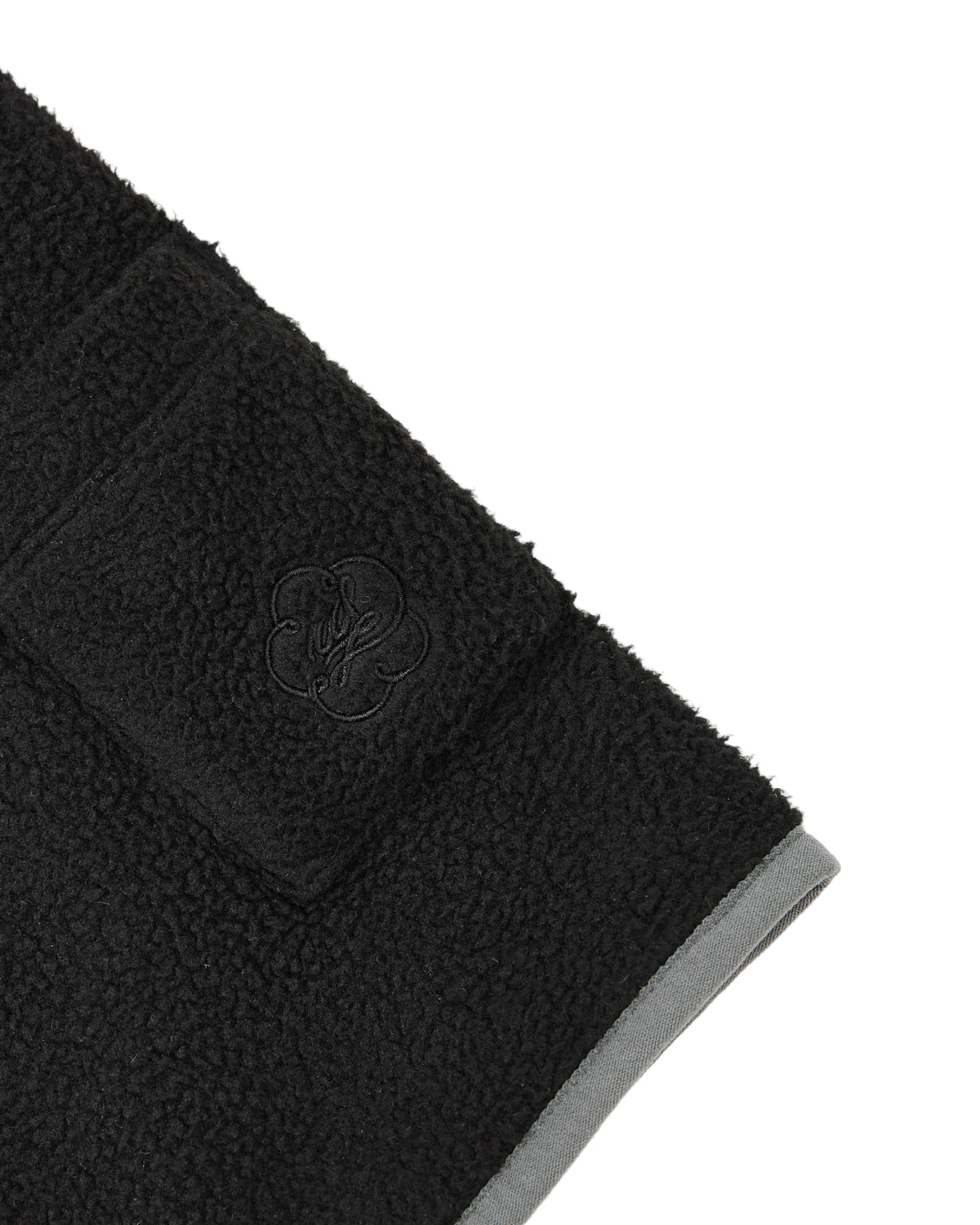 Close-up of the BLACK TEARDROP KNOT FLEECE by Sundae School—a cozy, East Asian inspired black fleece featuring a small pocket and an embossed logo. The edge is finished with a gray trim, adding a refined touch to this stylish piece.