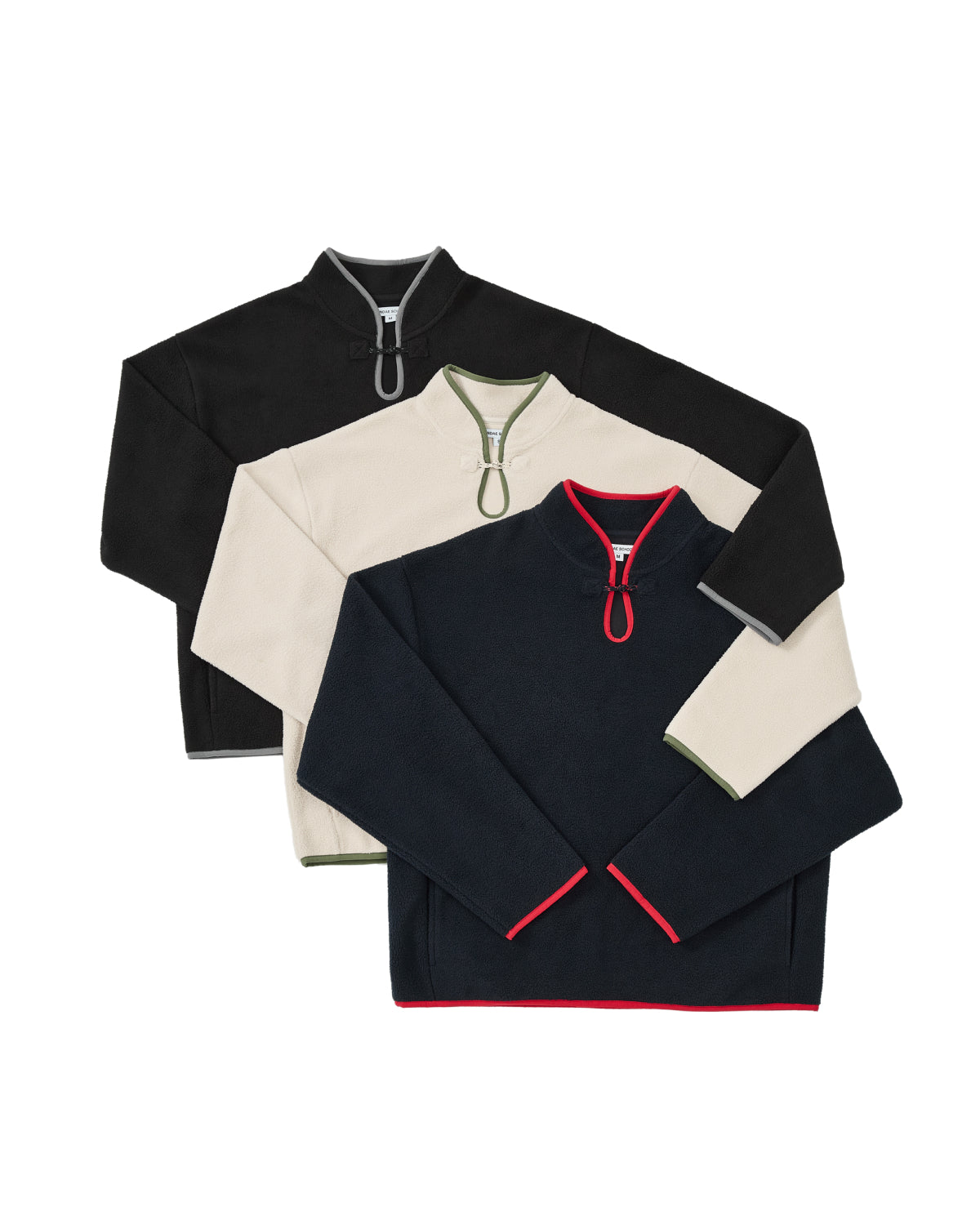 Three quarter-zip fleece pullovers are stacked. The top is the BLACK TEARDROP KNOT FLEECE by Sundae School, a cozy black fleece with a gray zipper; the middle is cream with green accents, and the bottom is navy with red trim and zipper detail.