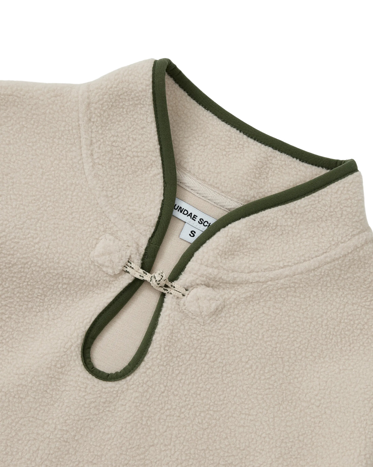 Close-up of the Sundae School TAUPE TEARDROP KNOT FLEECE, a cozy fleece top accented with green trim around the collar and keyhole opening, featuring a signature Teardrop Knot Fleece closure and a visible inner label.