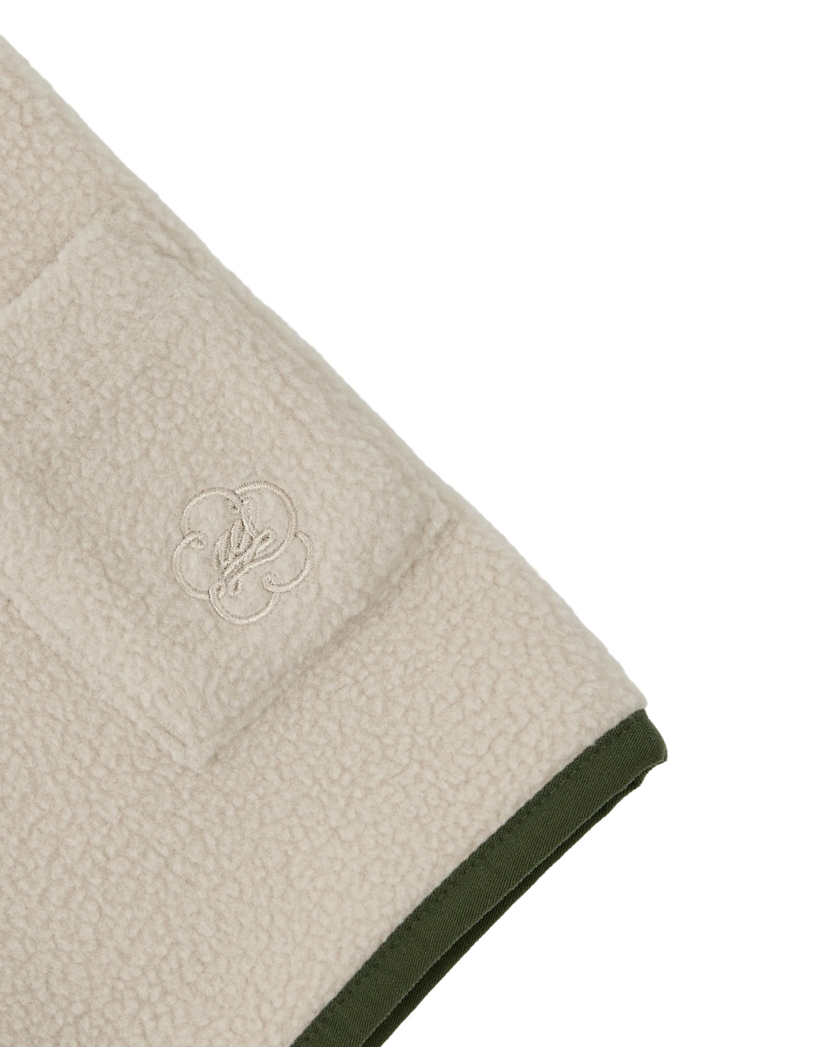 A close-up of the TAUPE TEARDROP KNOT FLEECE by Sundae School shows cozy fleece fabric with a pocket and an embroidered logo, accented by dark green trim along the edges. This piece features subtle East Asian-inspired details for a distinctive touch.