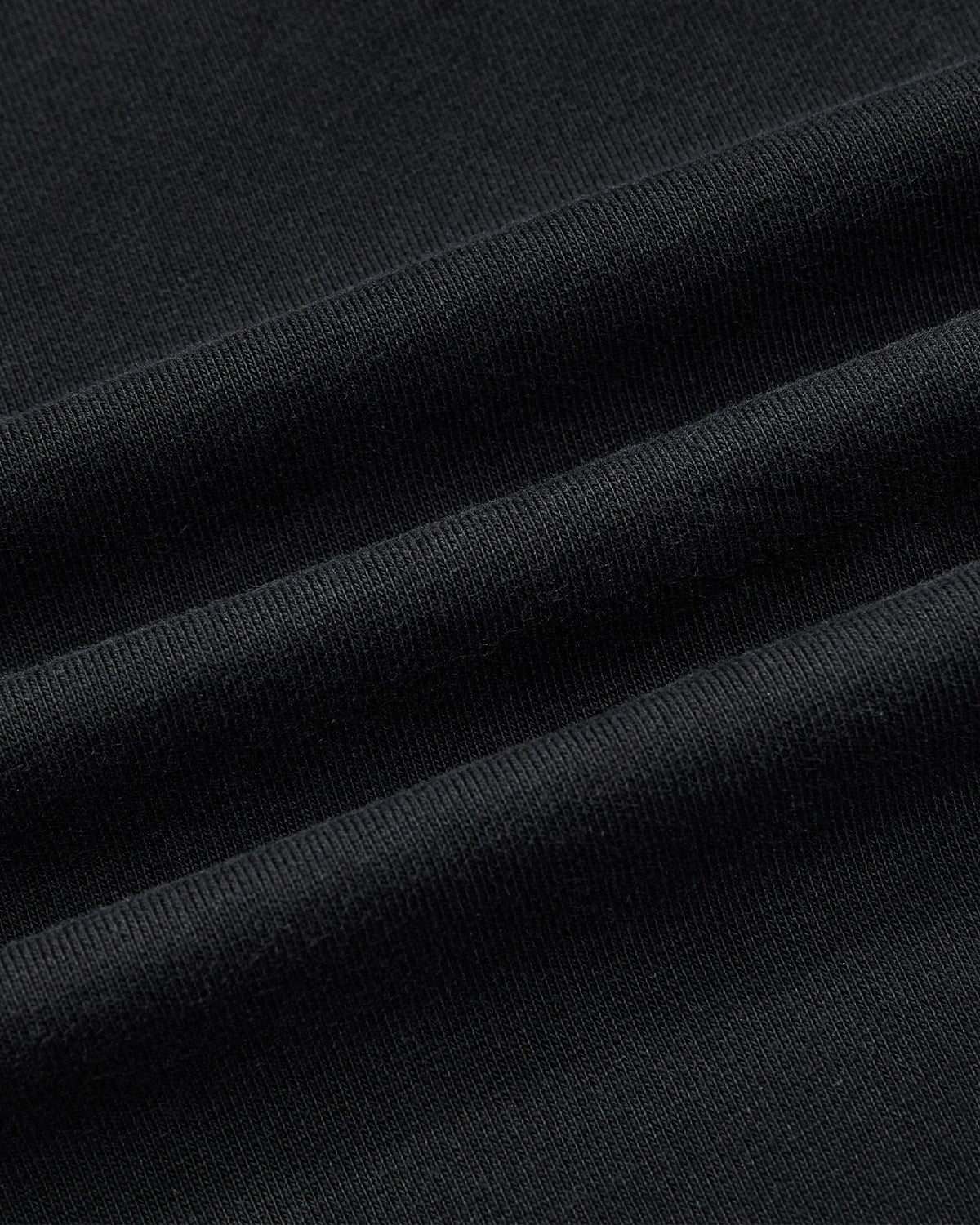 A close-up of the BLACK TEARDROP KNOT SWEATSHIRT by Sundae School, featuring folded black cotton fabric with a soft texture and fine weave that highlights the visible ridges.