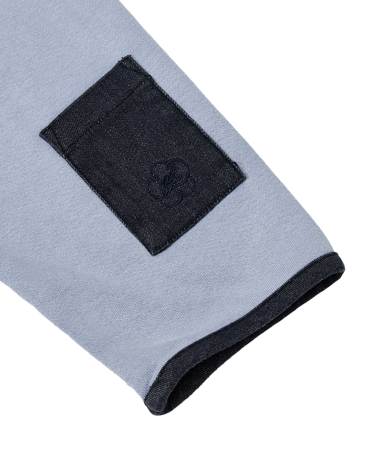 A close-up of the SKY BLUE TEARDROP KNOT SWEATSHIRT by Sundae School highlights a light blue sleeve with a dark denim pocket and cuff, both featuring denim trim. The 100% cotton sweatshirt’s pocket is adorned with an intricate embroidered teardrop design.