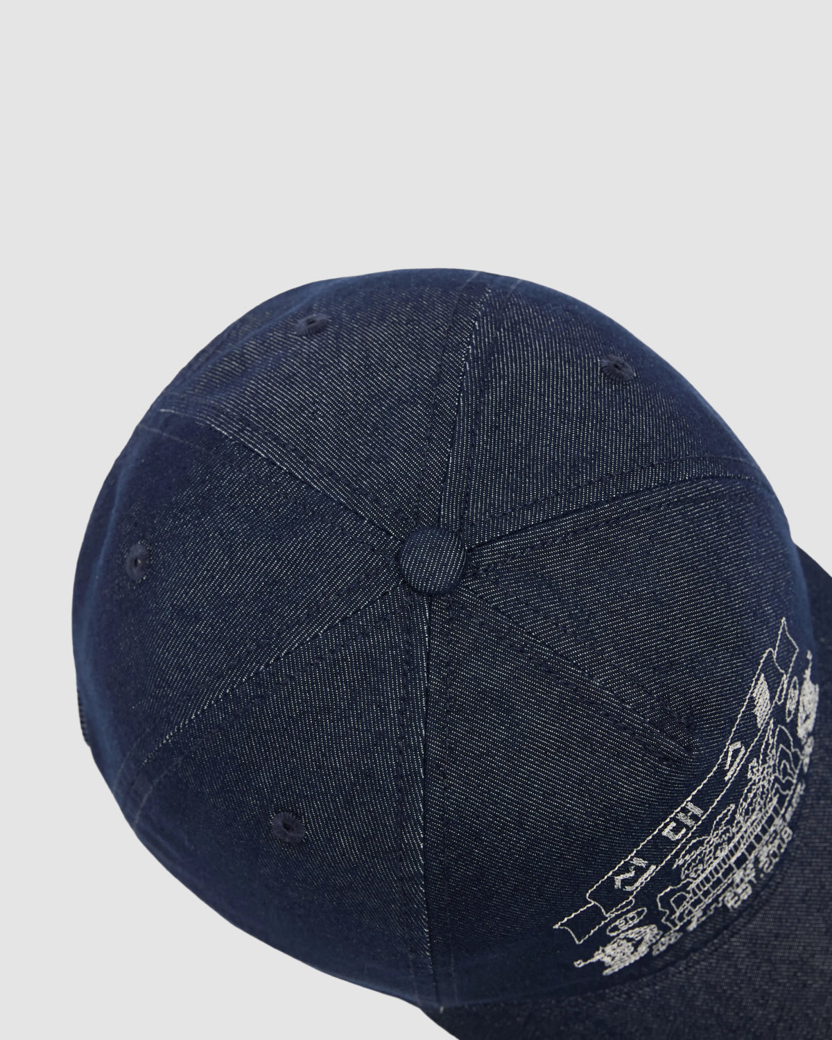 A close-up, overhead view of the Sundae School INDIGO DENIM TIGER CAP—a dark blue denim strapback hat with visible stitching and partial white graphic text on the brim—set against a plain light background.