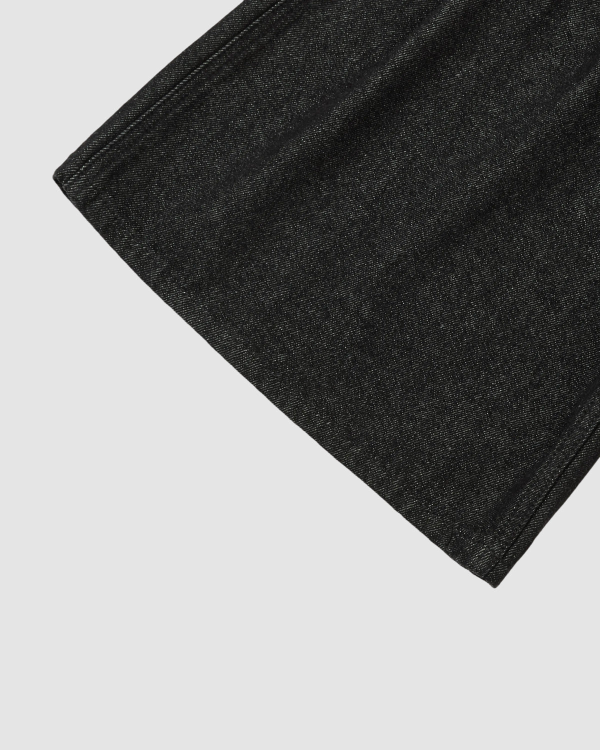 Close-up of the hem and fabric of Sundae School BLACK VITA JORTS, dark charcoal grey in color, displayed on a light grey background.