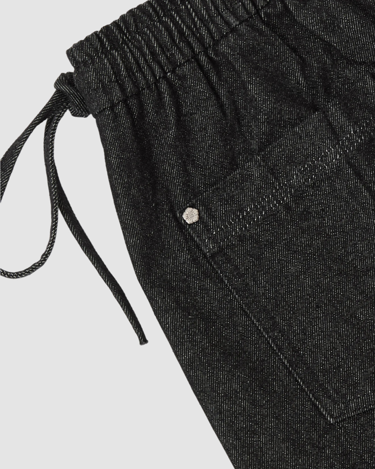 Close-up of Sundae School BLACK VITA JORTS featuring a black elastic waist, visible side pocket with silver rivet, and white stitching. The denim has a slight sheen and textured look, giving these jorts a modern edge.