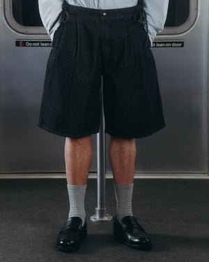 A person stands on a subway, wearing Sundae School BLACK VITA JORTS, light gray socks, and black loafers. Only their lower half is visible against a backdrop of a metal subway door with a warning sign.