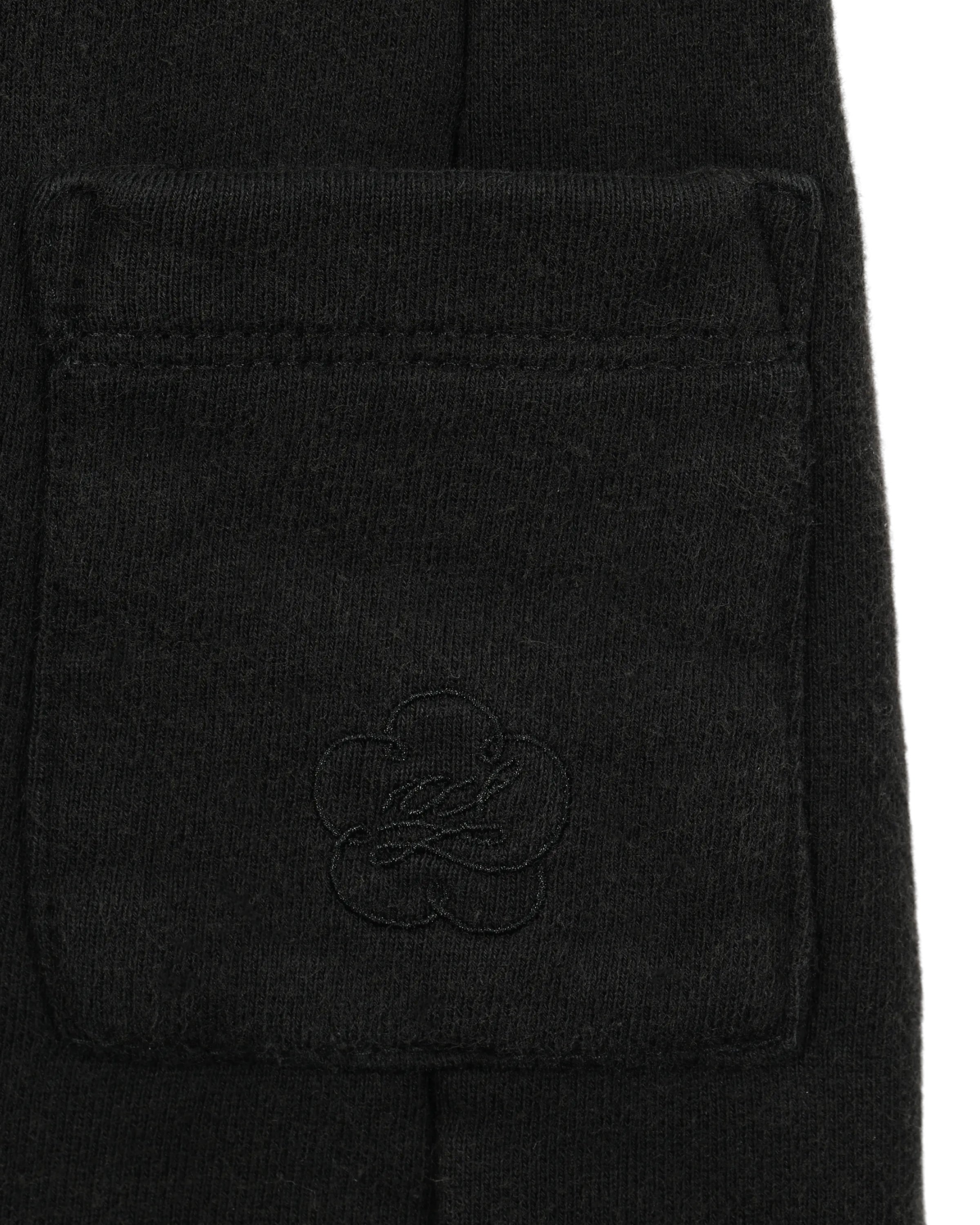 Close-up of the BLACK WASH WRAP SWEAT BAJI by Sundae School, showcasing a black fabric pocket with subtle embroidered flower and script details on its soft, high-quality cotton surface—reminiscent of unisex jogger sweatpants.