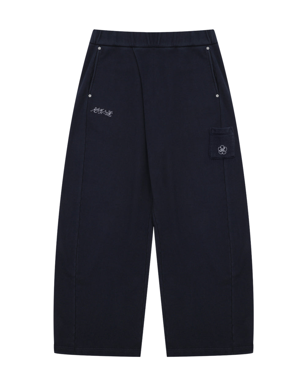 NAVY WASH WRAP SWEAT BAJI by Sundae School features a wide-leg unisex silhouette in black, an elastic waistband, two front pockets with button closures, subtle white embroidered text on one side, and a flap pocket adorned with a flower patch on the other.