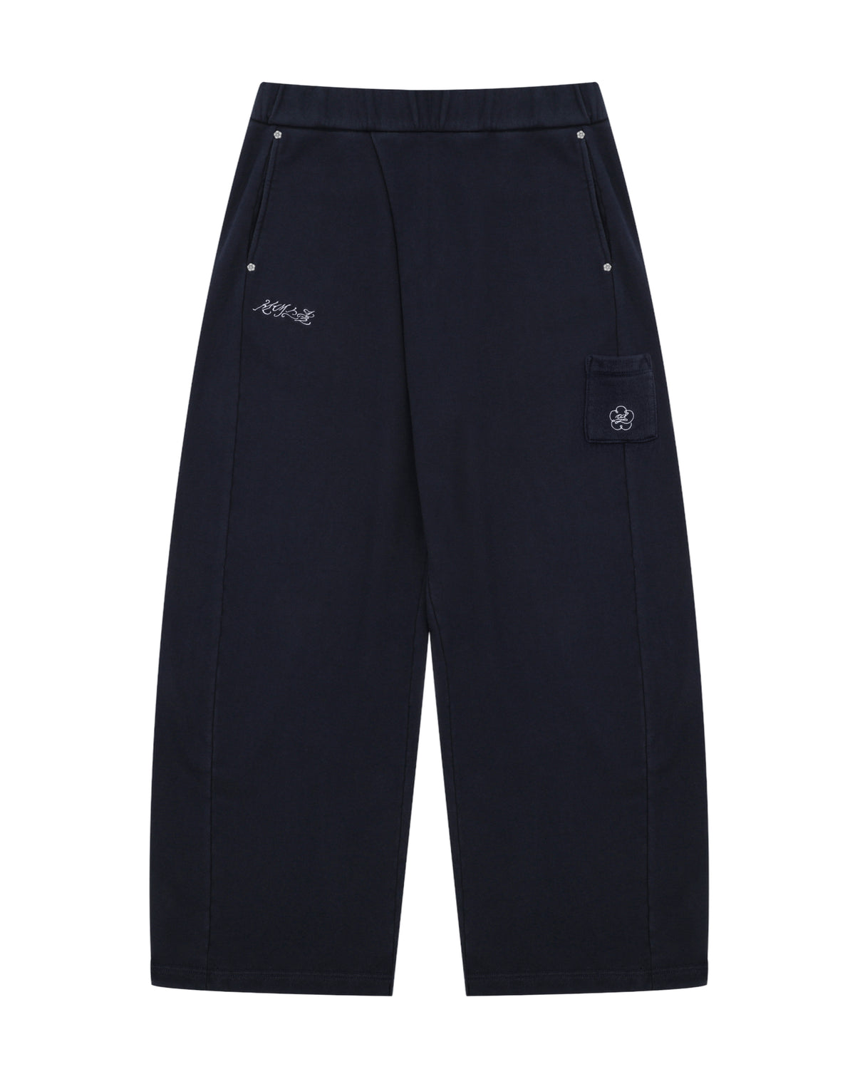 NAVY WASH WRAP SWEAT BAJI by Sundae School features a wide-leg unisex silhouette in black, an elastic waistband, two front pockets with button closures, subtle white embroidered text on one side, and a flap pocket adorned with a flower patch on the other.