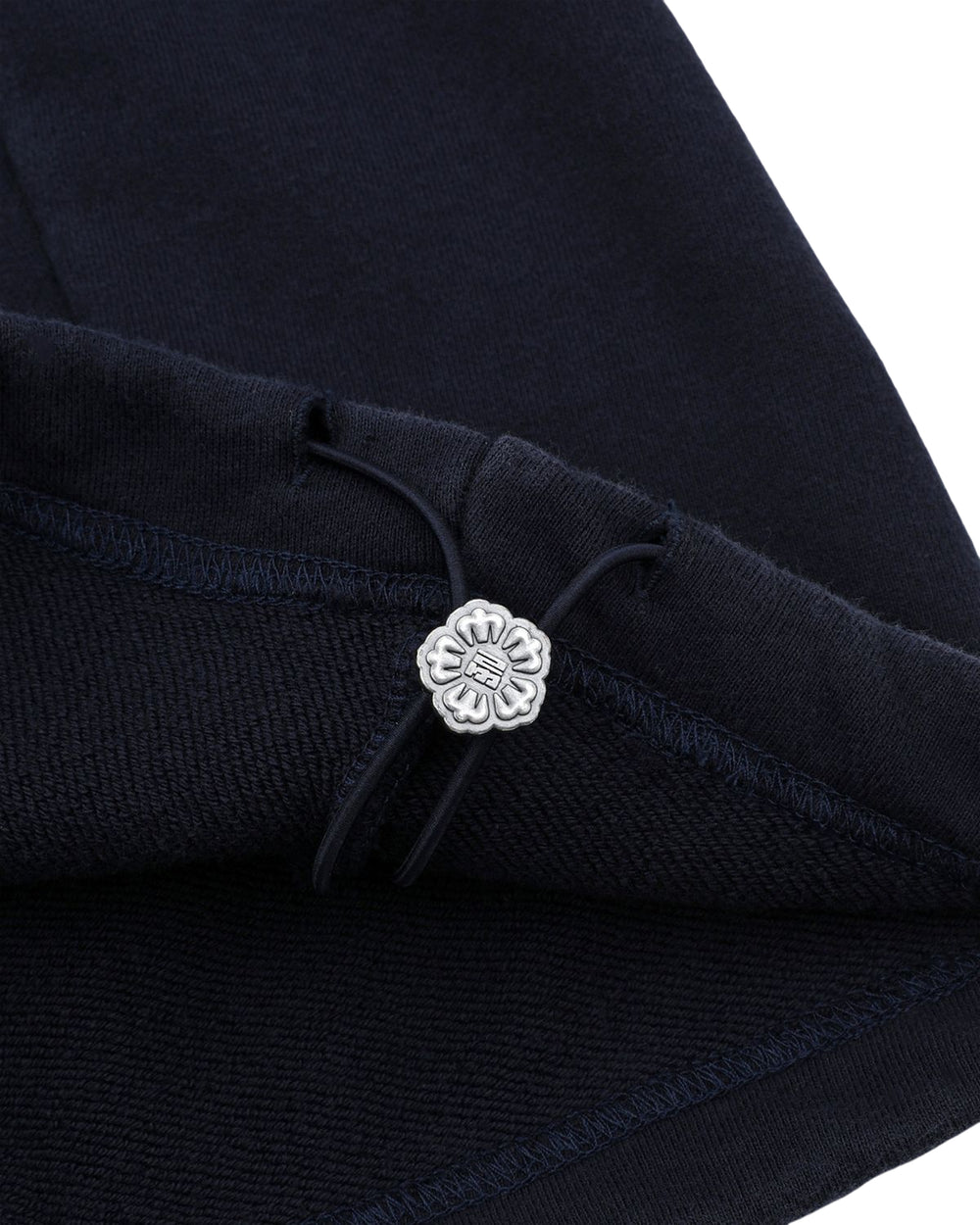 Close-up of the dark navy fabric from Sundae School's NAVY WASH WRAP SWEAT BAJI, featuring a silver flower-shaped button and black drawstring detail, highlighting the stitching and texture.