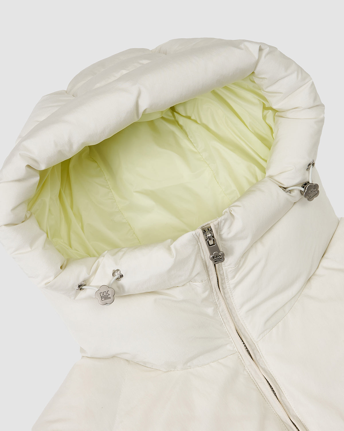 Close-up of the Sundae School IVORY LIME ORIGAMI PUFFER, a white puffer jacket with a hood lined in light yellow, front zipper, and metallic drawstring stoppers.