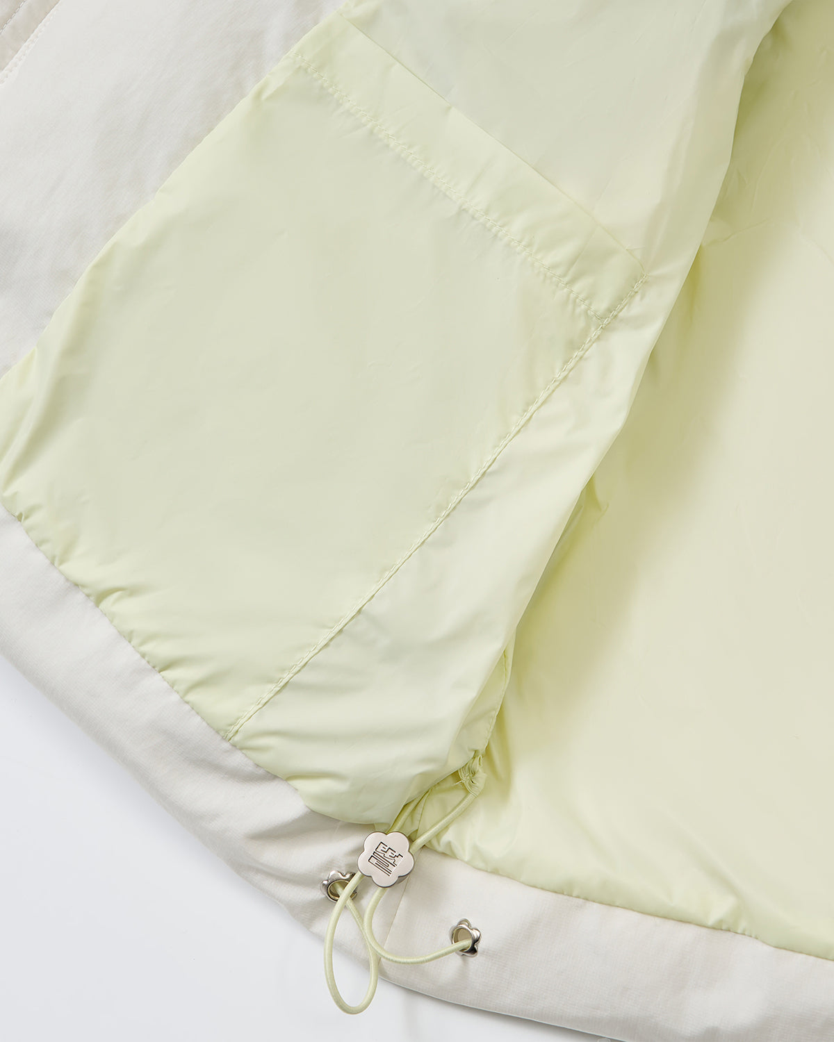 Close-up of the inside of the Sundae School IVORY LIME ORIGAMI PUFFER, featuring a pale yellow lining, interior pocket, and an adjustable drawstring with metal toggle at the hem.