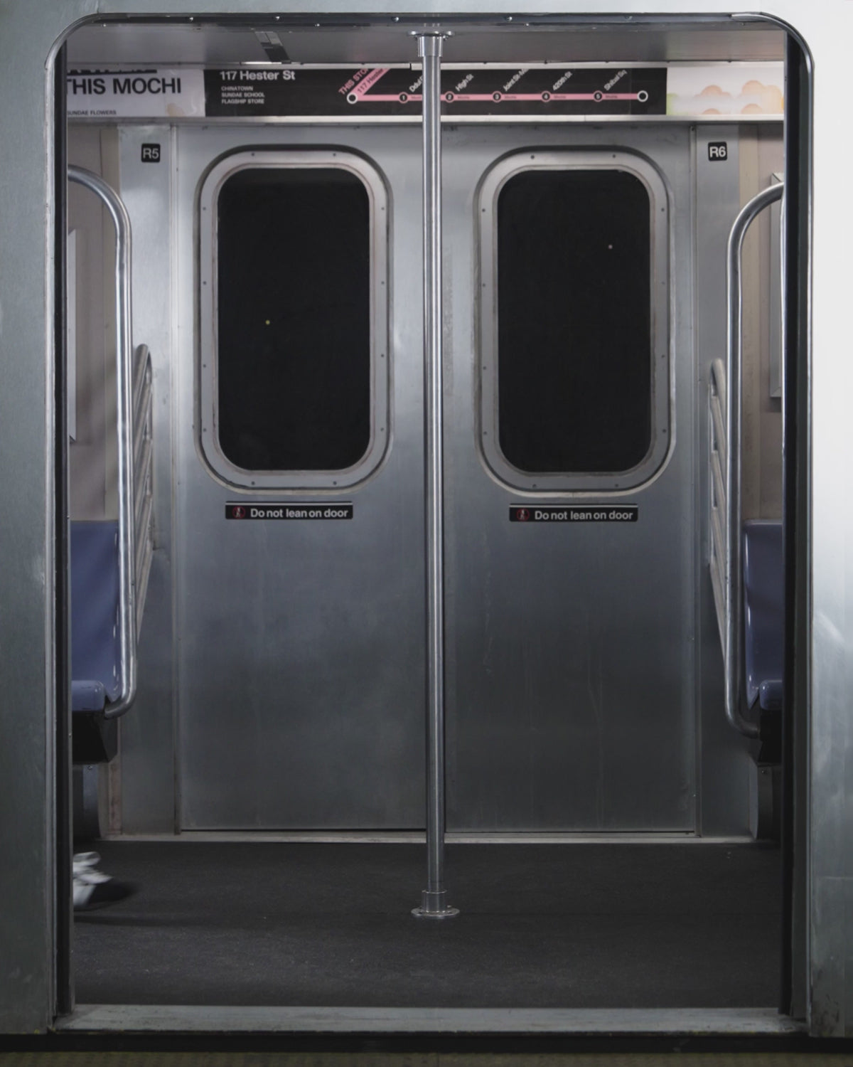 A woman with long dark hair and sunglasses wears the Sundae School NAVY OFFICE QUARTER ZIP, light blue tie, and dark shorts as she stands by subway doors beneath a map and a “117 Hester St” sign.