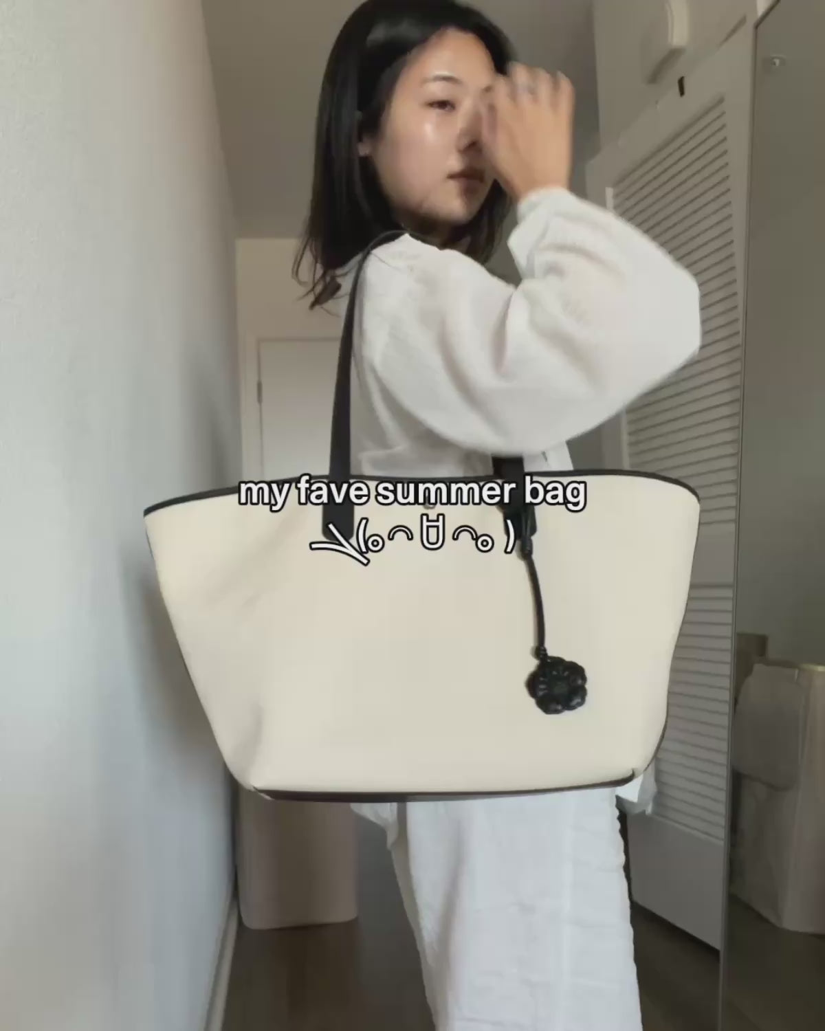 A video demonstrating how to pack and style a cream-colored Sundae School canvas tote bag trimmed in black. A person packs everyday essentials like a tablet, planner, journal, Mochi gummies, and sunglasses into the bag's organized compartments, then models different ways to wear and carry the tote.