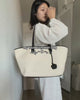 A video demonstrating how to pack and style a cream-colored Sundae School canvas tote bag trimmed in black. A person packs everyday essentials like a tablet, planner, journal, Mochi gummies, and sunglasses into the bag's organized compartments, then models different ways to wear and carry the tote.